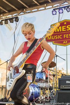 a woman playing guitar on stage at an outdoor music festival in front of a sign that says mes music festival