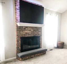 a flat screen tv mounted above a brick fireplace in a living room with white walls