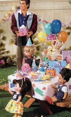 there is a birthday cake on the table with many dolls around it and balloons in the background