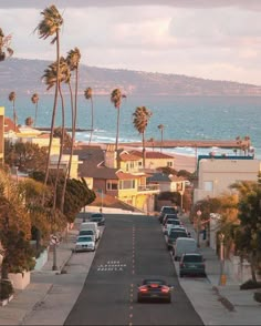 cars are parked on the side of an empty street near the ocean and palm trees