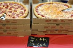 two pizzas sitting in boxes on top of a red table cloth covered tablecloth