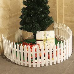 a white picket fence with a christmas tree in the middle and presents wrapped around it