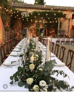 a long table with candles and flowers on it is set for an outdoor dinner party