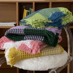 a stack of blankets sitting on top of a chair in front of a book shelf