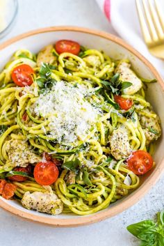 a white bowl filled with pasta and meat covered in pesto, cheese and tomatoes