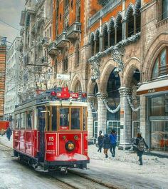 a red trolley car traveling down a snow covered street