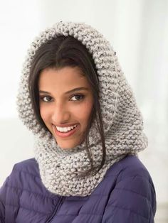 a smiling woman wearing a knitted cowl with hood on her head and scarf around her neck