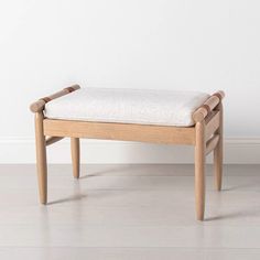 a wooden bench with a white cushion on the seat and backrest, in front of a white wall