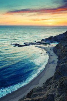 the sun is setting over the ocean with waves coming in from the shore and sand on the beach