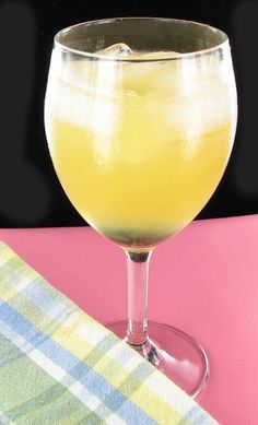 a glass filled with yellow liquid sitting on top of a pink tablecloth next to a napkin