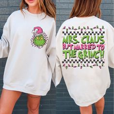 two women wearing matching sweatshirts that say mrs claus but married to the grin