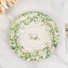 a white plate with green leaves and flowers on it next to a fork and knife