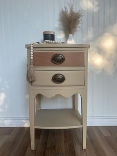 a white table with two drawers and a vase on top, sitting in front of a wall