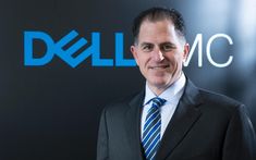 a man wearing a suit and tie standing in front of a dell inc sign with the company's logo on it