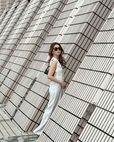 a woman standing in front of a building with sunglasses on her head and leaning against the wall