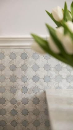 a vase filled with white flowers sitting on top of a counter next to a wall