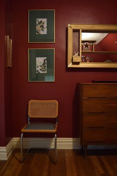 a chair sitting next to a dresser in a room with red walls and pictures on the wall