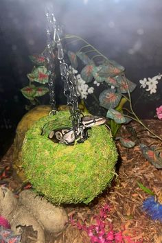 a moss ball hanging from a chain with scissors on it and flowers in the background