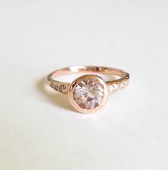 a pink diamond ring sitting on top of a white surface with diamonds around the band