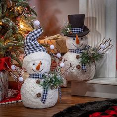 two snowmen with hats and scarfs are sitting in front of a christmas tree