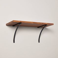 a wooden shelf sitting on top of a wall next to two black metal brackets and a white wall