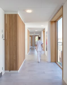 a man in white walking down a long hallway with wood paneling on the walls