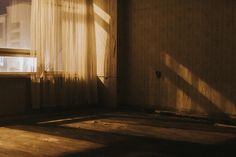 an empty room with sunlight coming through the window and curtains on the windowsills