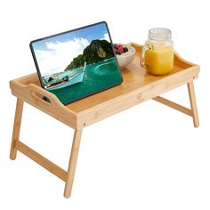 a wooden table with a laptop, bowl of fruit and glass of orange juice on it