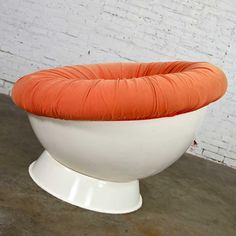 an orange and white chair sitting on top of a cement floor next to a brick wall