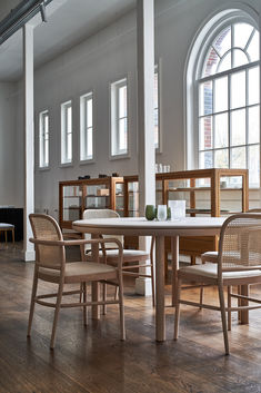 a table and chairs in a room with large windows on the wall, next to a book shelf