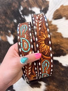 a woman's hand holding two brown and turquoise leather bracelets