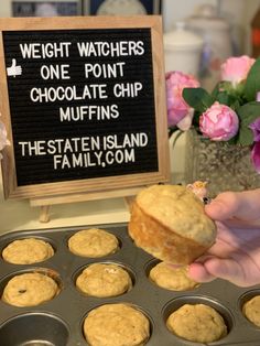 a person holding a muffin in front of a sign