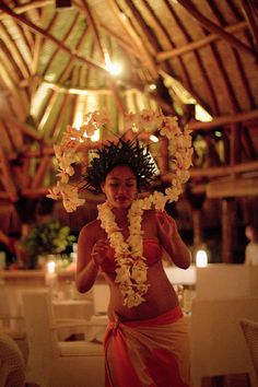 a woman with flowers in her hair standing under a wooden structure holding a hula skirt