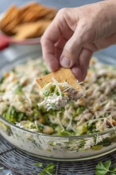 a person dipping a cracker into a bowl of broccoli and cheese salad