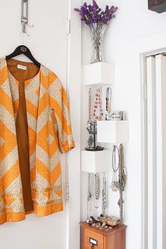 an orange and white jacket hanging on a wall next to a vase with purple flowers