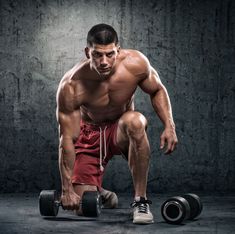 a man squatting down with two dumbbells in front of him