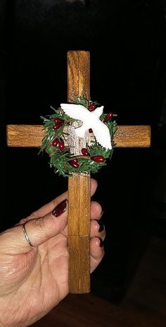 a hand holding a wooden cross with a wreath on it and a white dove in the center