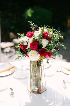 a vase filled with red and white flowers sitting on top of a table next to plates