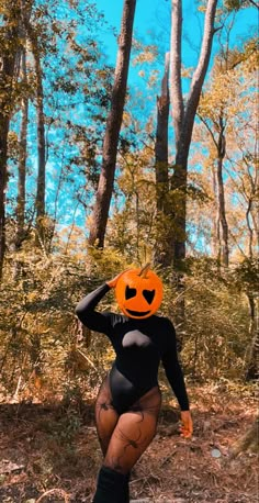 a woman in a black bodysuit with an orange pumpkin on her head walking through the woods