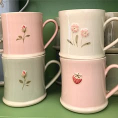 three coffee mugs with flowers and hearts painted on them sitting next to each other