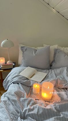 two lit candles sit on top of a bed with blue and white striped sheets,