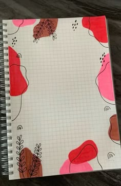 a spiral notebook with red and pink flowers on it, sitting on a table next to a pen