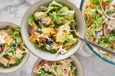 four bowls filled with salad on top of a marble countertop next to a glass bowl full of salad