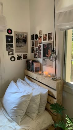 a bed with white sheets and pillows next to a window filled with pictures on the wall