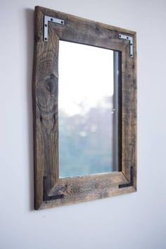 a wooden mirror hanging on the wall next to a white wall with a window in it