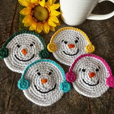 three crocheted snowmen sitting next to a coffee cup and sunflowers