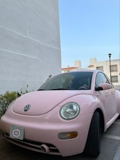 a pink volkswagen beetle parked in front of a white building on the side of the road