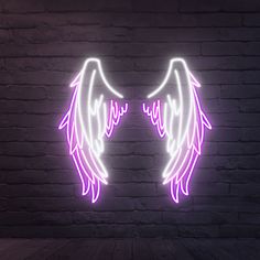 an angel wings neon sign on a brick wall