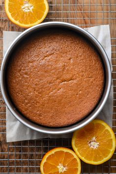 an orange cake in a pan on a cooling rack with sliced oranges around it