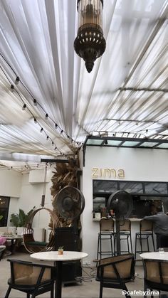 the inside of a restaurant with tables and chairs under a white sheeted ceiling that has lights hanging from it